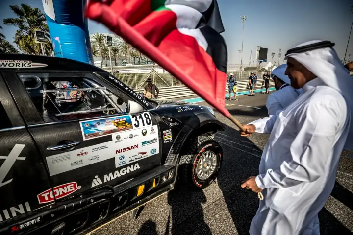 Abu Dhabi Desert Challenge 2018: official waving UAE flag beside race car