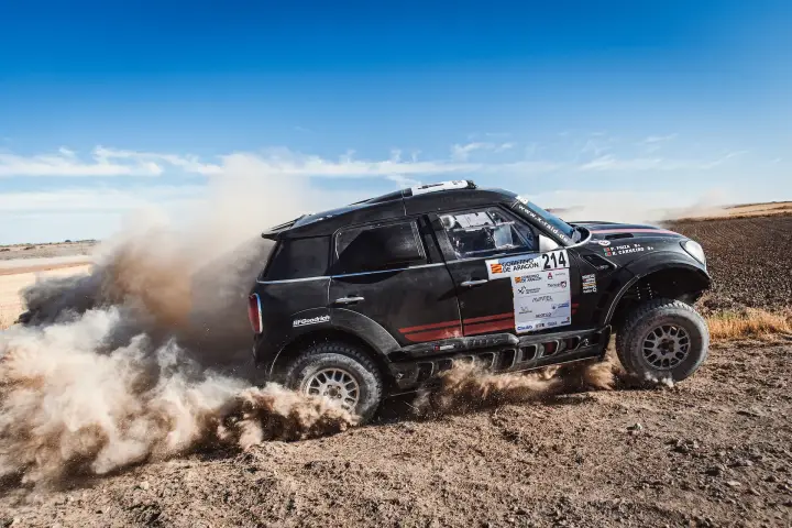 Baja Aragón 2021: dark Mini drifting broadside on flat dusty terrain