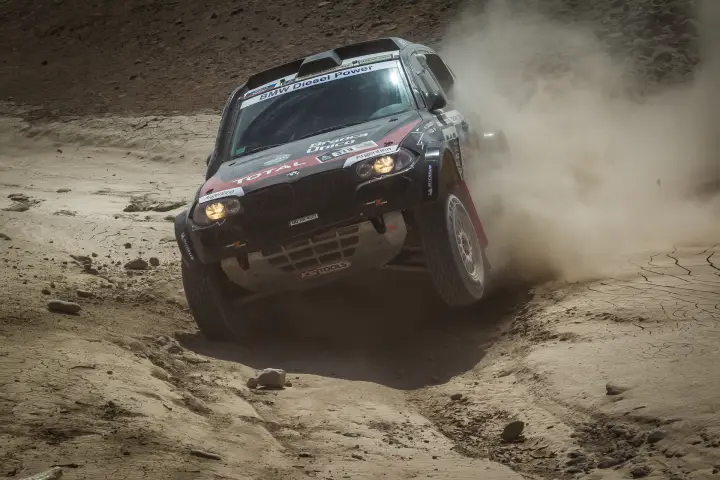 Dakar Rally 2013: BMW climbing steep rocky desert hill dust