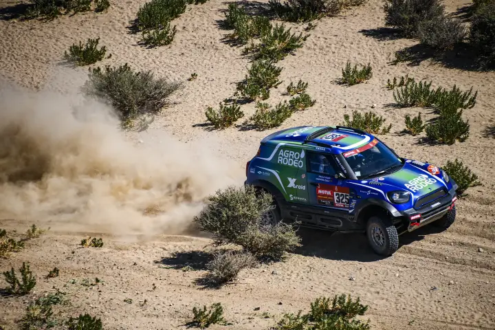 Dakar Rally 2021: blue Mini racing through desert shrubland kicking dust
