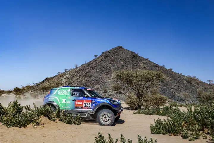Dakar Rally 2021: blue Mini passing rocky hill in desert landscape