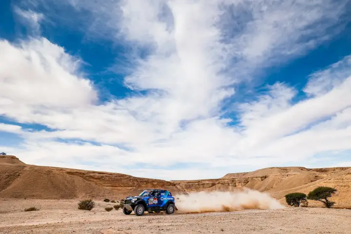 Dakar Rally 2022: blue rally car racing through rocky desert