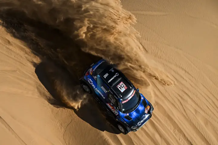 Dakar Rally 2022: aerial view car climbing sand dune clouds