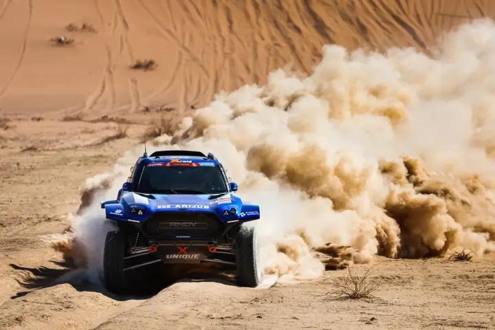 Dakar Rally 2024: blue buggy speeding past sandy desert dunes