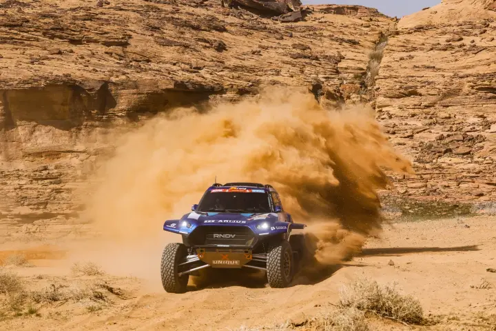 Dakar Rally 2024: rally car blasting through narrow rock canyon dust