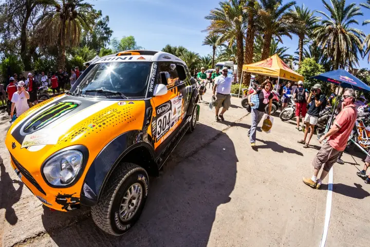 Rallye du Maroc 2013: orange Mini surrounded by crowd under palm trees