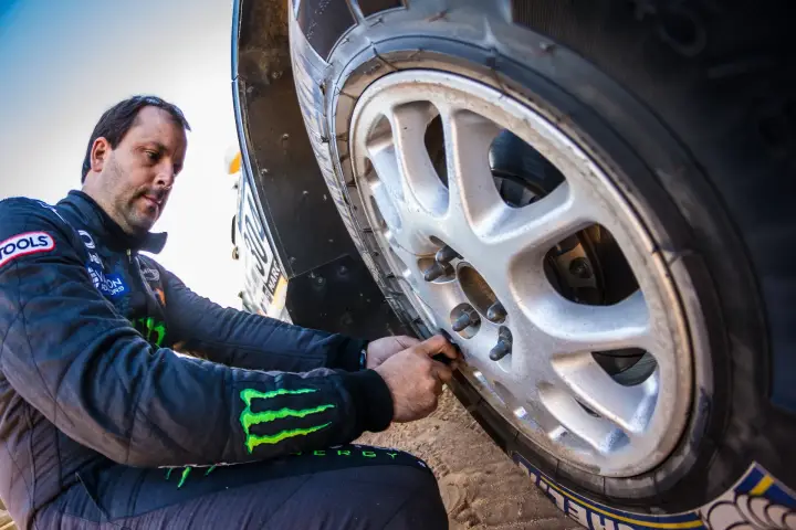 Rallye du Maroc 2013: driver changing tire on rally car in desert