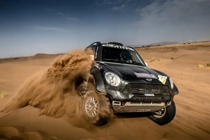Rallye du Maroc 2016: black Mini attacking dune kicking up sand spray