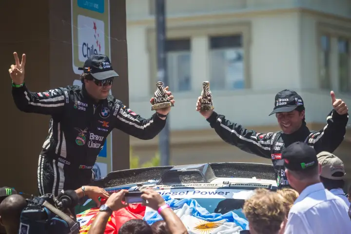 Pódio: two drivers on car roof holding Dakar trophies